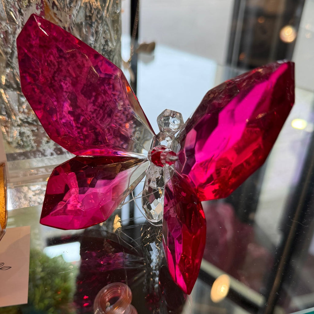 Deep magenta faceted crystal butterfly on a glass shelf