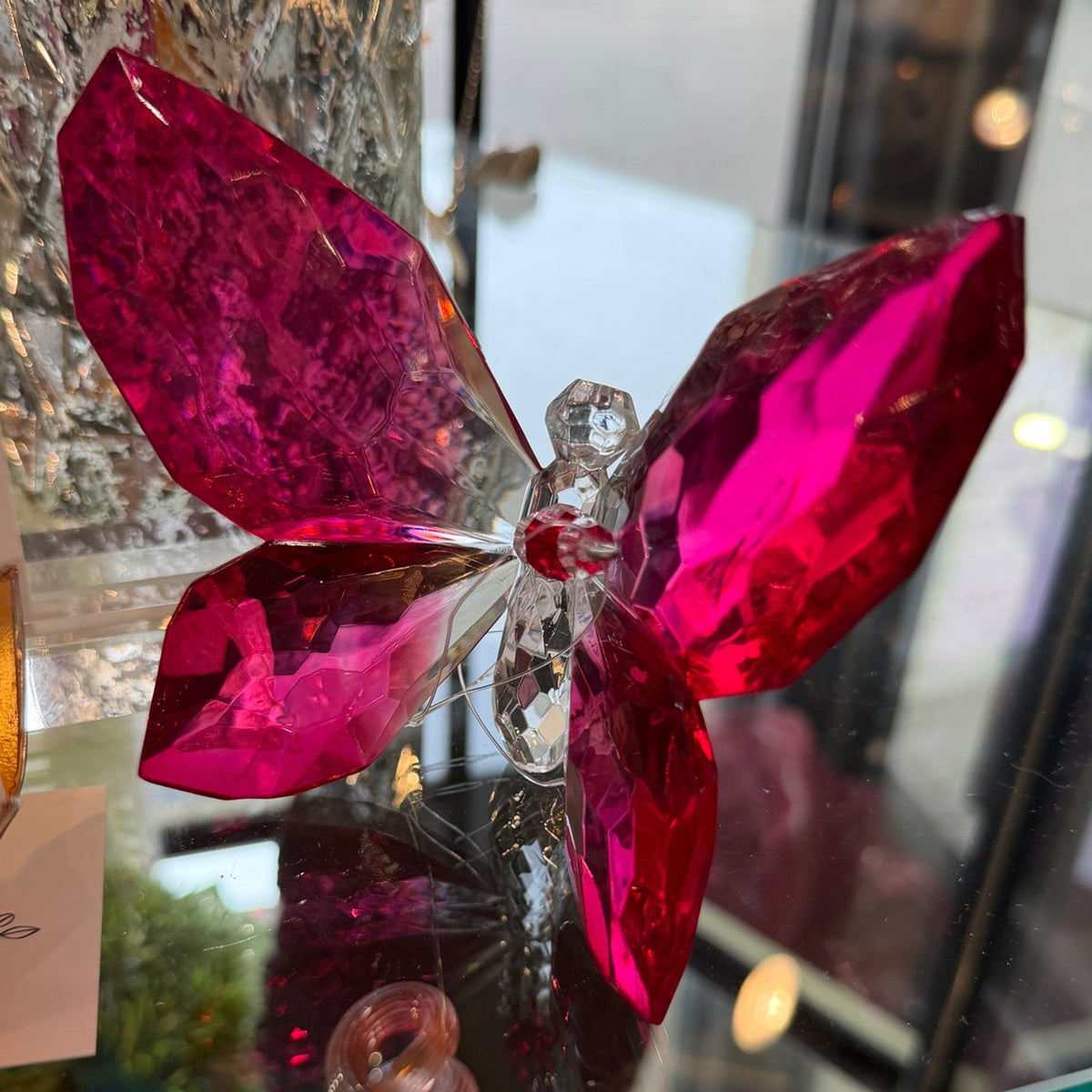 Deep magenta faceted crystal butterfly on a glass shelf