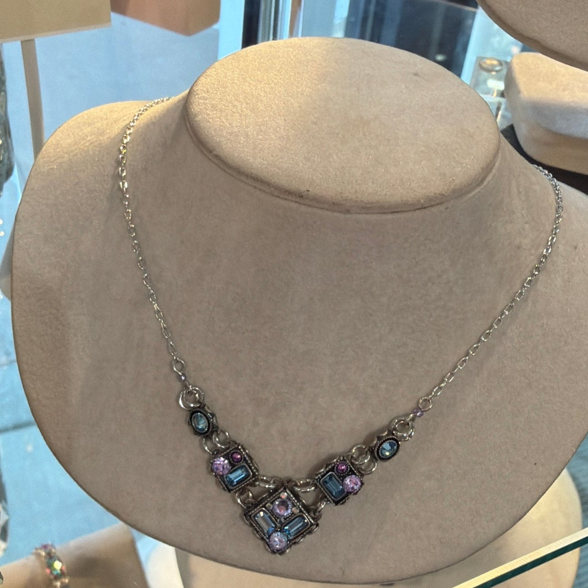 V-shaped necklace of square links with light blue and lavender crystals on a beige bust