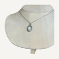 Oval opalescent white pendant with crystal halo on a silver chain, shown on a beige bust