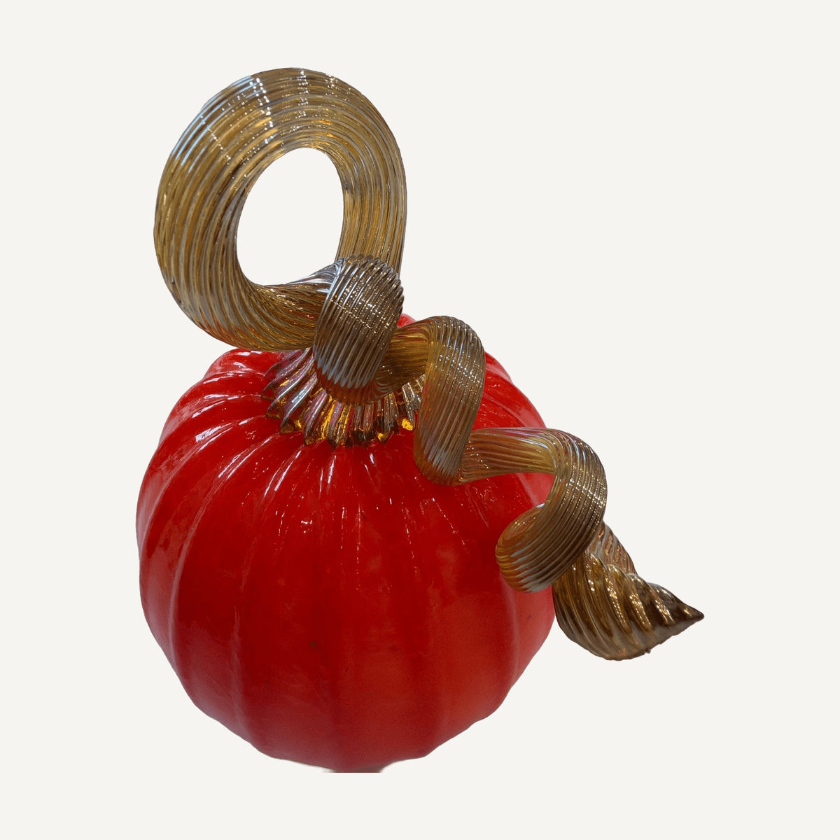 Orange ribbed glass pumpkin with a tall looping amber glass stem on a white table