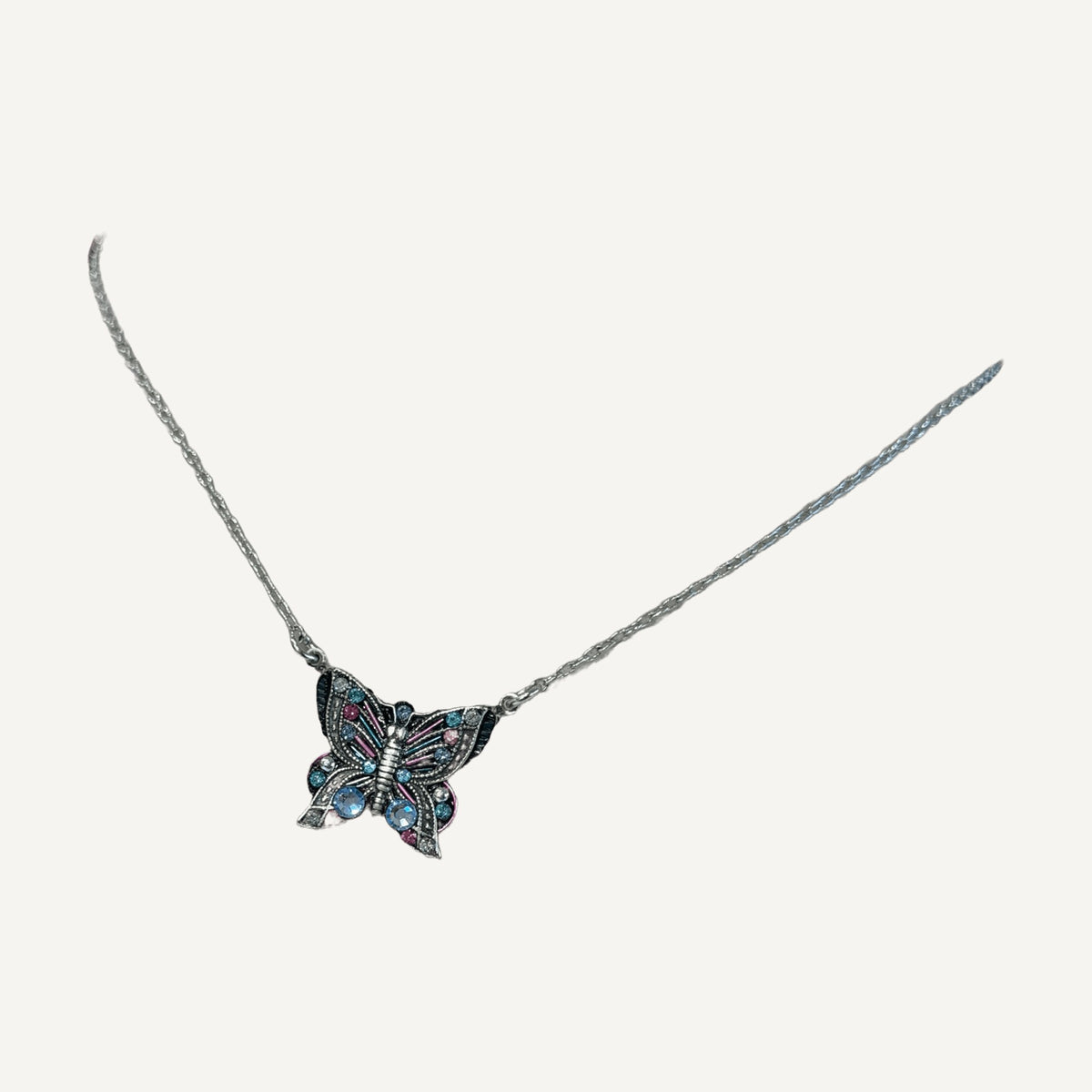 Butterfly pendant necklace with blue and pink crystals on a gray velvet bust